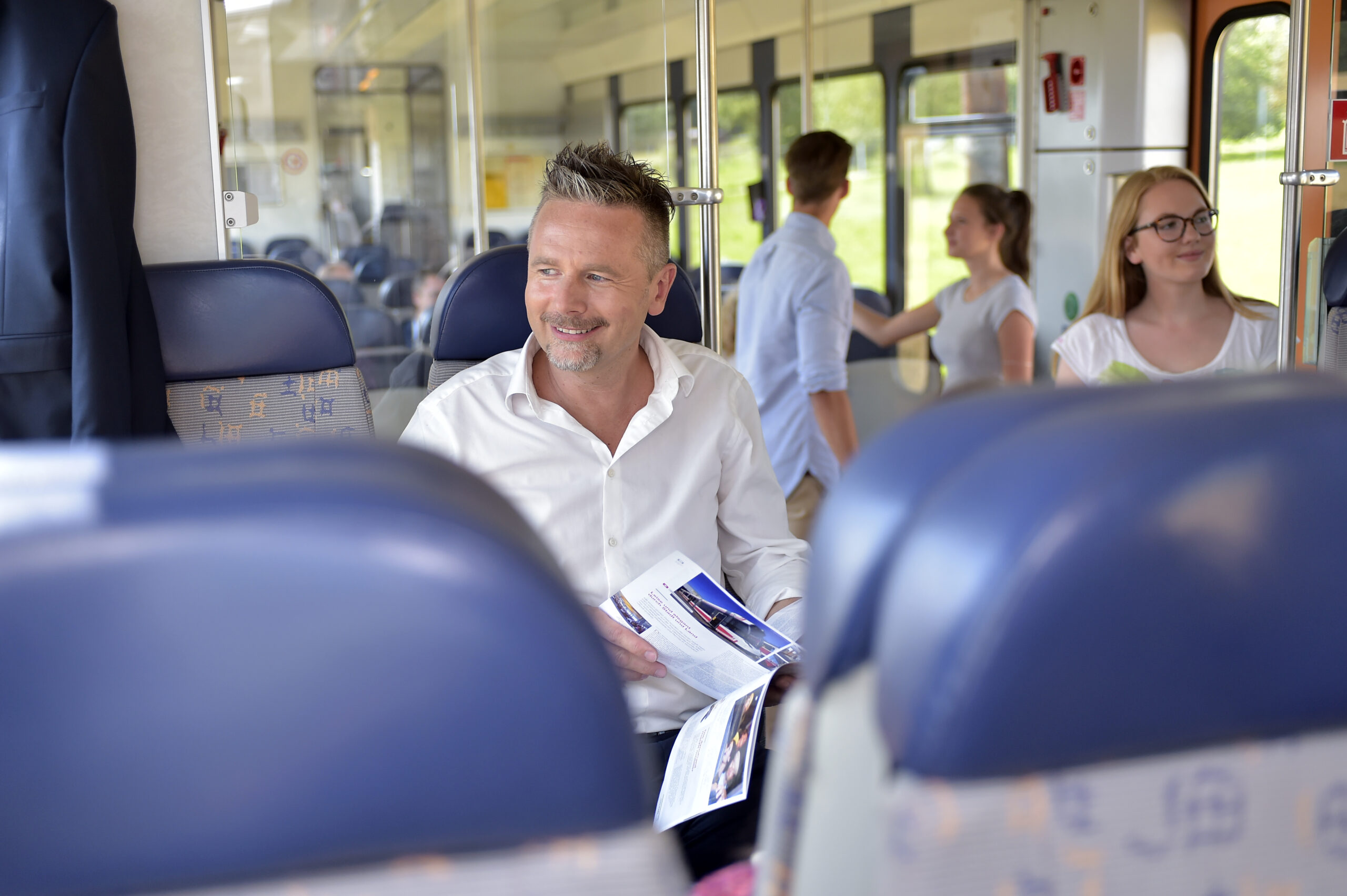 Ein Mann sitzt in einer LILO und sieht beim Fenster hinaus und liest dabei eine Zeitschrift